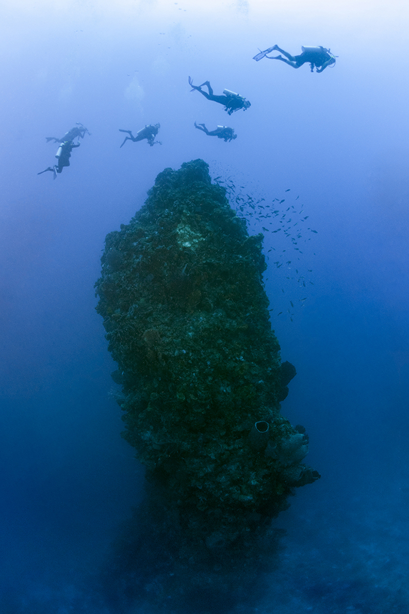 Divers swimming over the top of the Eye of the Needle in Saba, Eastern Caribbean.